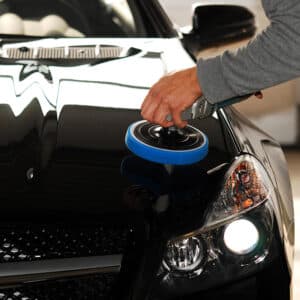 Main polissant le capot noir d'une voiture avec une polisseuse. La carrosserie est ultra brillante, sans défauts.