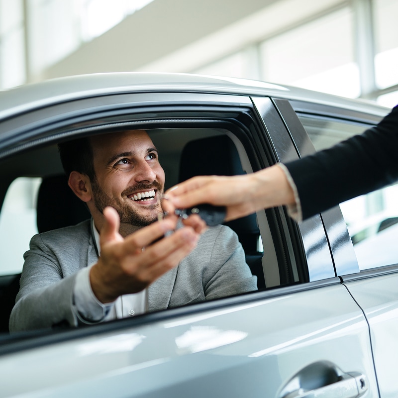 Homme souriant reçoit les clés d'une voiture neuve d'un vendeur. Scène de remise de clés à un client dans une concession automobile.