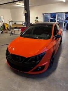 Voiture Seat Ibiza orange vif et toit noir dans un atelier de covering. Phares et calandre noirs, jantes sombres, sticker 'starfobag'.